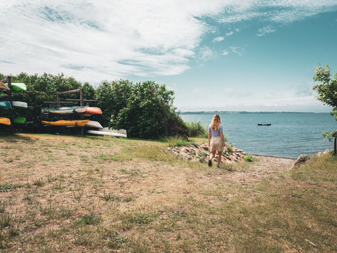 Frau geht auf eine kleine sandige Bucht am Meer zu, daneben liegen Kanus